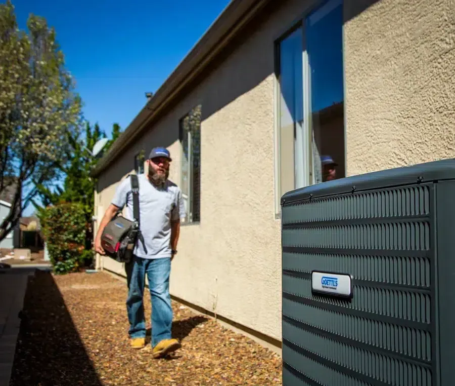 Goettl’s High Desert Mechanical technician walking along side yard toward outdoor HVAC unit – Prescott Valley AZ